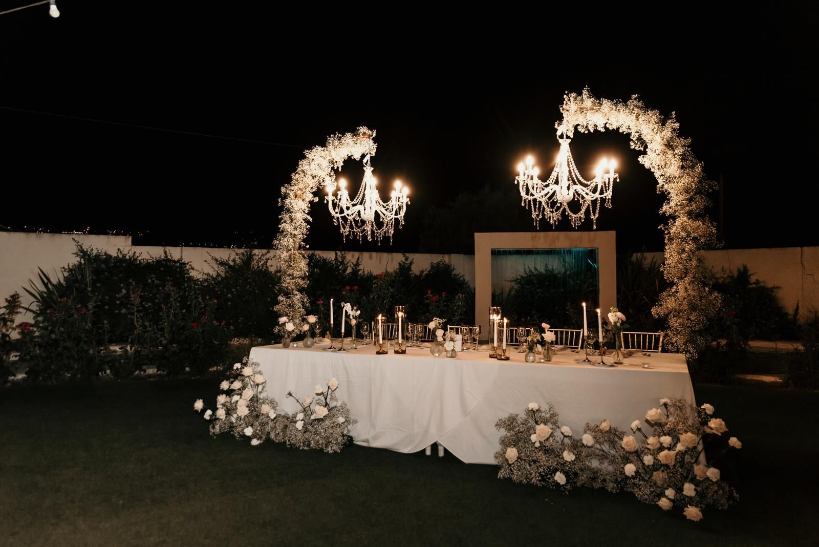 Una mesa larga blanca con velas y flores por la noche.
