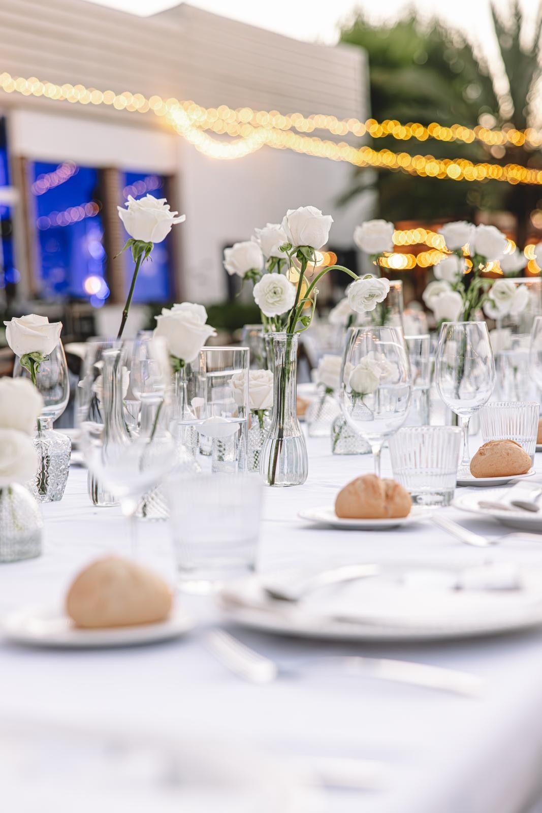 Una mesa preparada para una recepción de boda con platos, vasos y jarrones con flores.