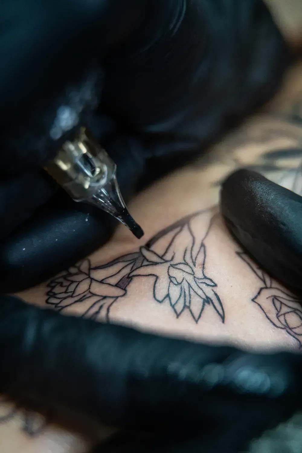 Máquina de tatuar dibujando un diseño floral en la piel con manos enguantadas cerca