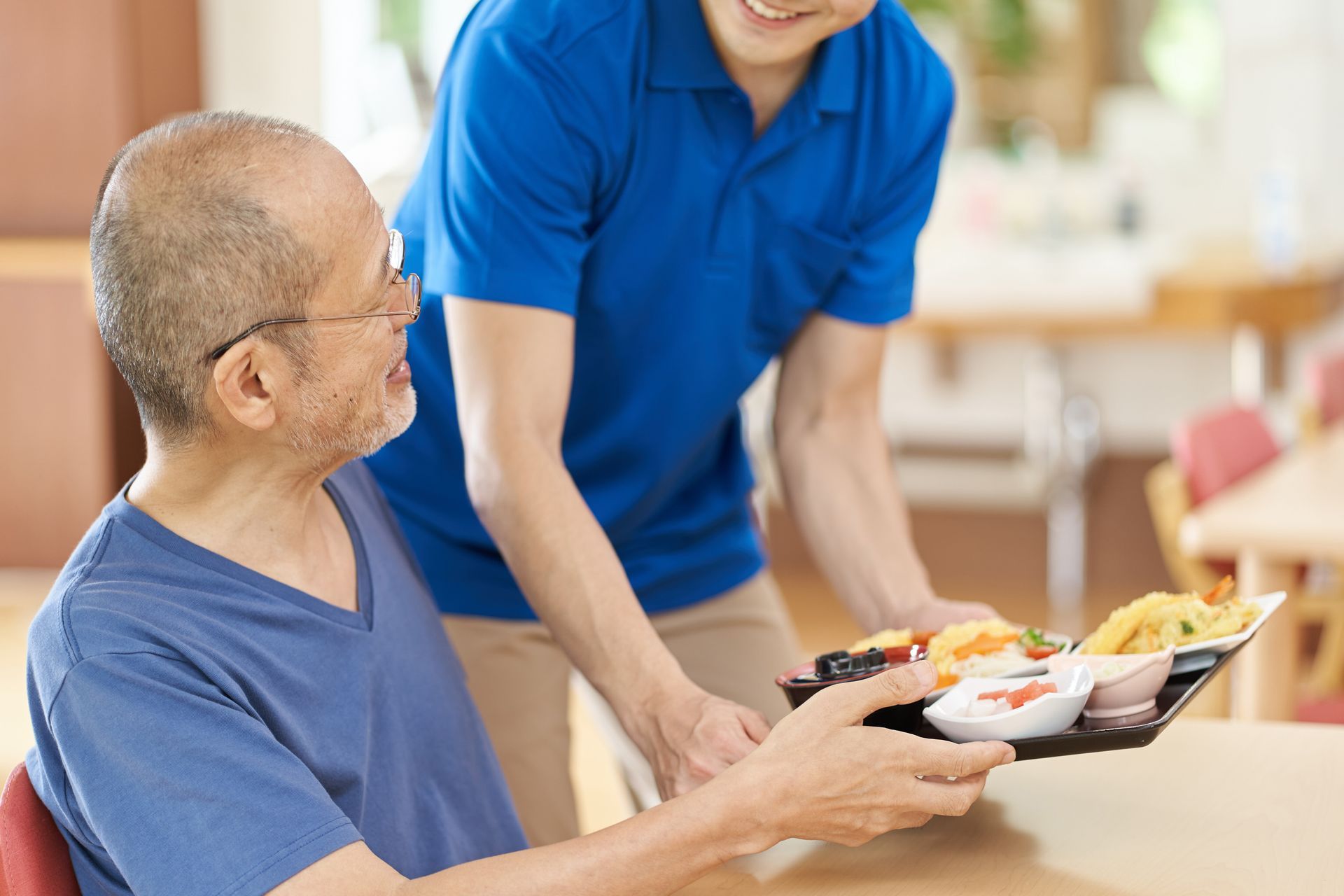Un soignant sert un repas à un homme âgé dans une salle à manger. Tous deux sourient.