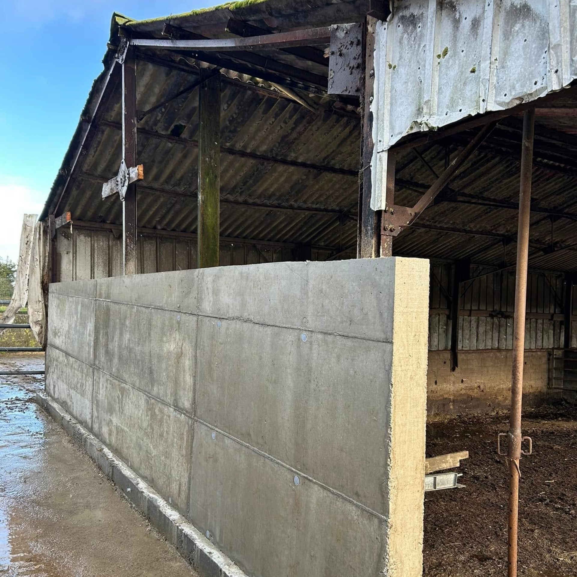 Mur en parpaings sous un toit de grange délabré dans un hangar agricole ouvert