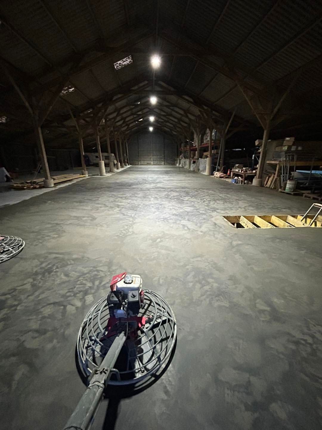 Intérieur d'entrepôt sombre avec une autolaveuse au premier plan et des lumières zénithales s'estompant au loin.