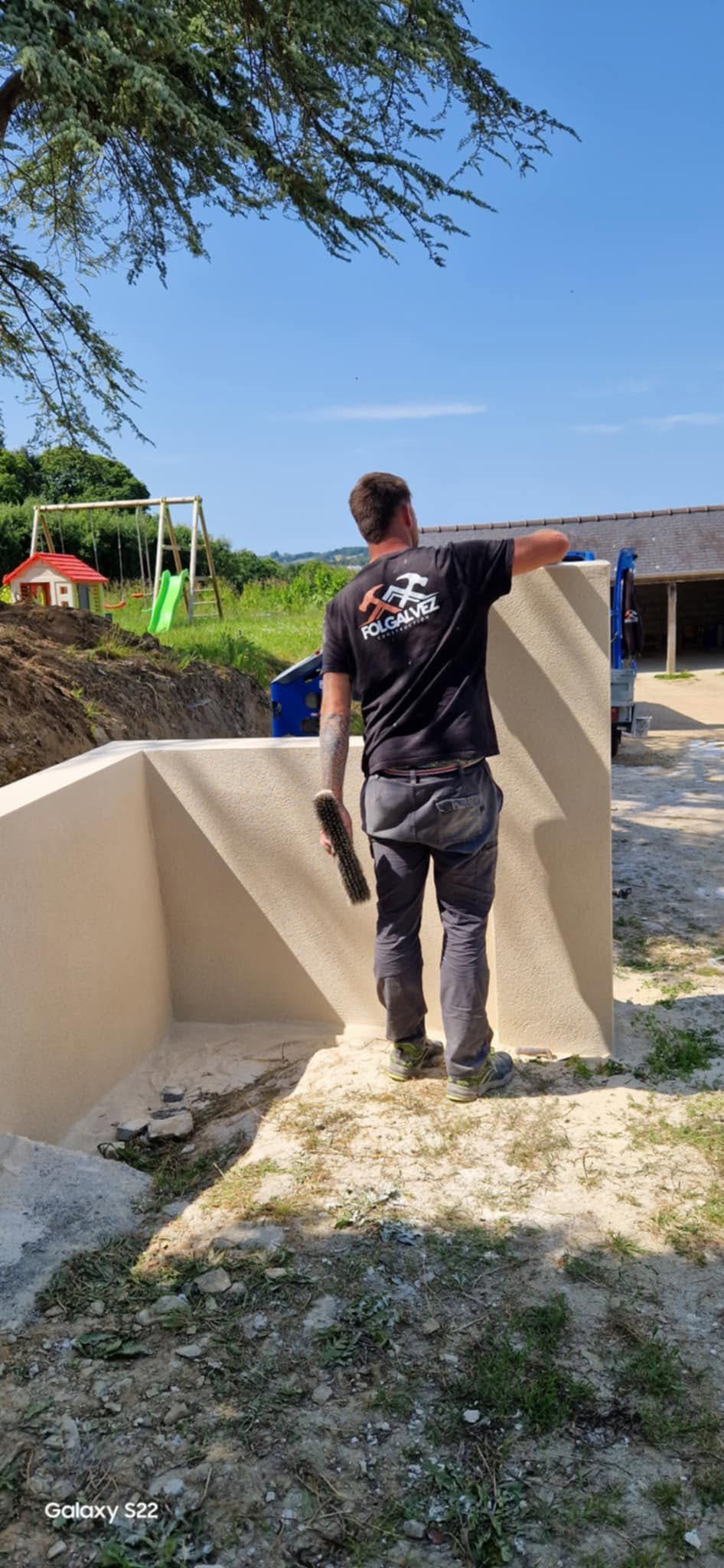 Une personne se tient entre des murs de béton sur un sentier rocailleux en plein air sous un ciel bleu.