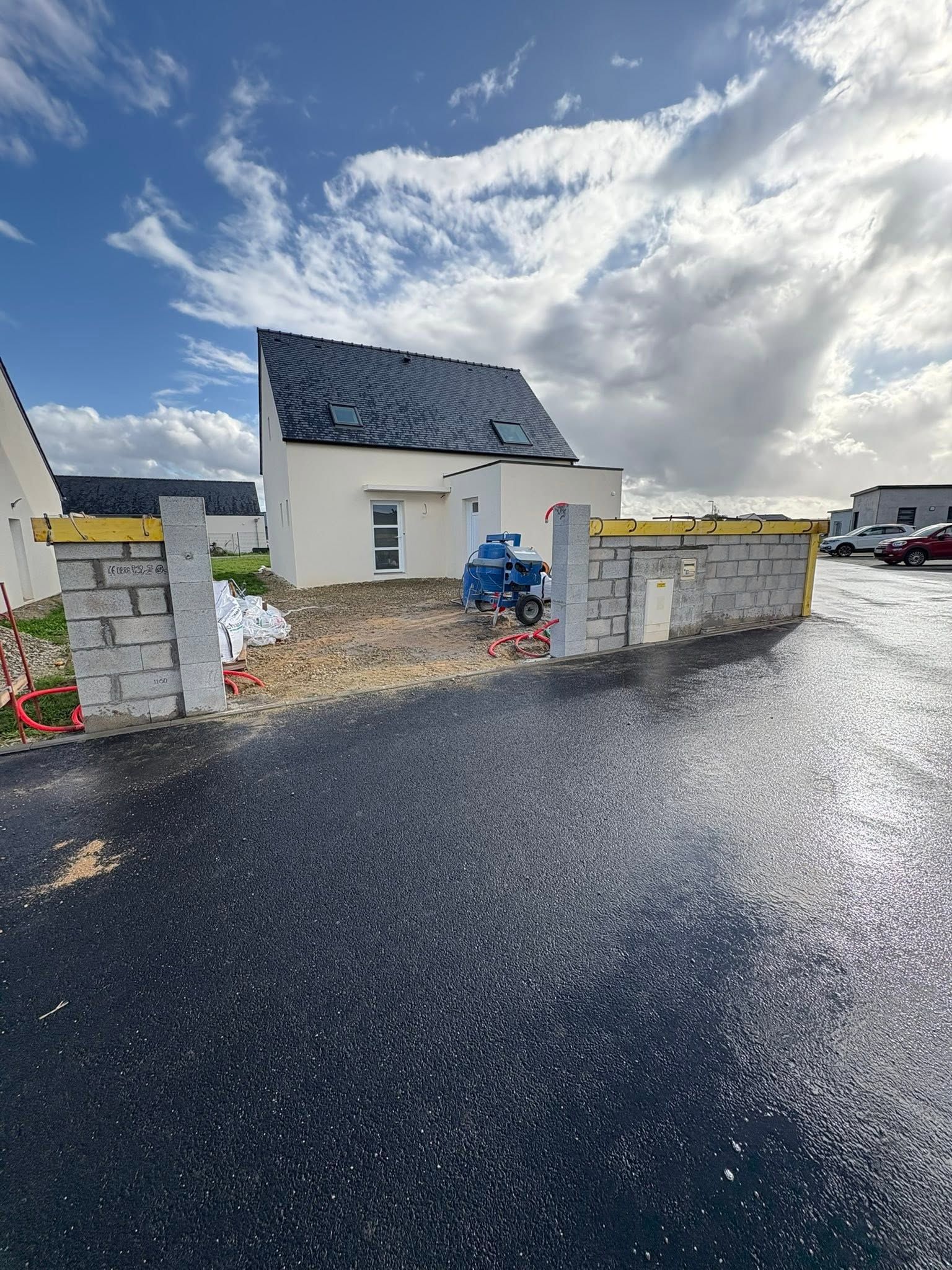 Maison neuve avec allée de gravier, murs blancs, toit en ardoise et ciel nuageux après la pluie