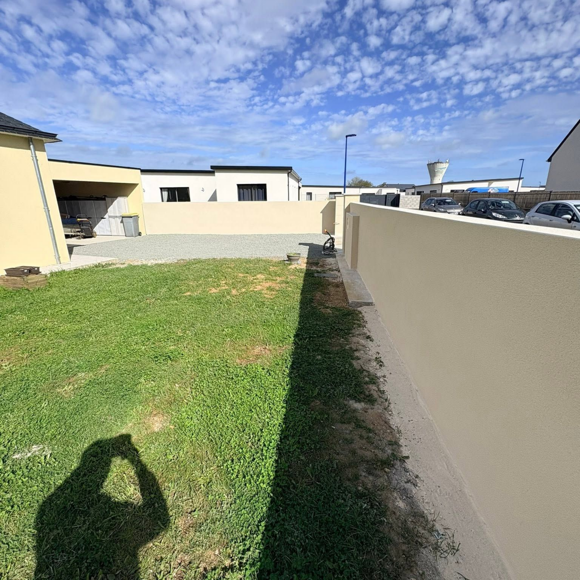 Jardin avec pelouse verte, des murs beiges et maisons blanches sous un ciel d'un bleu éclatant
