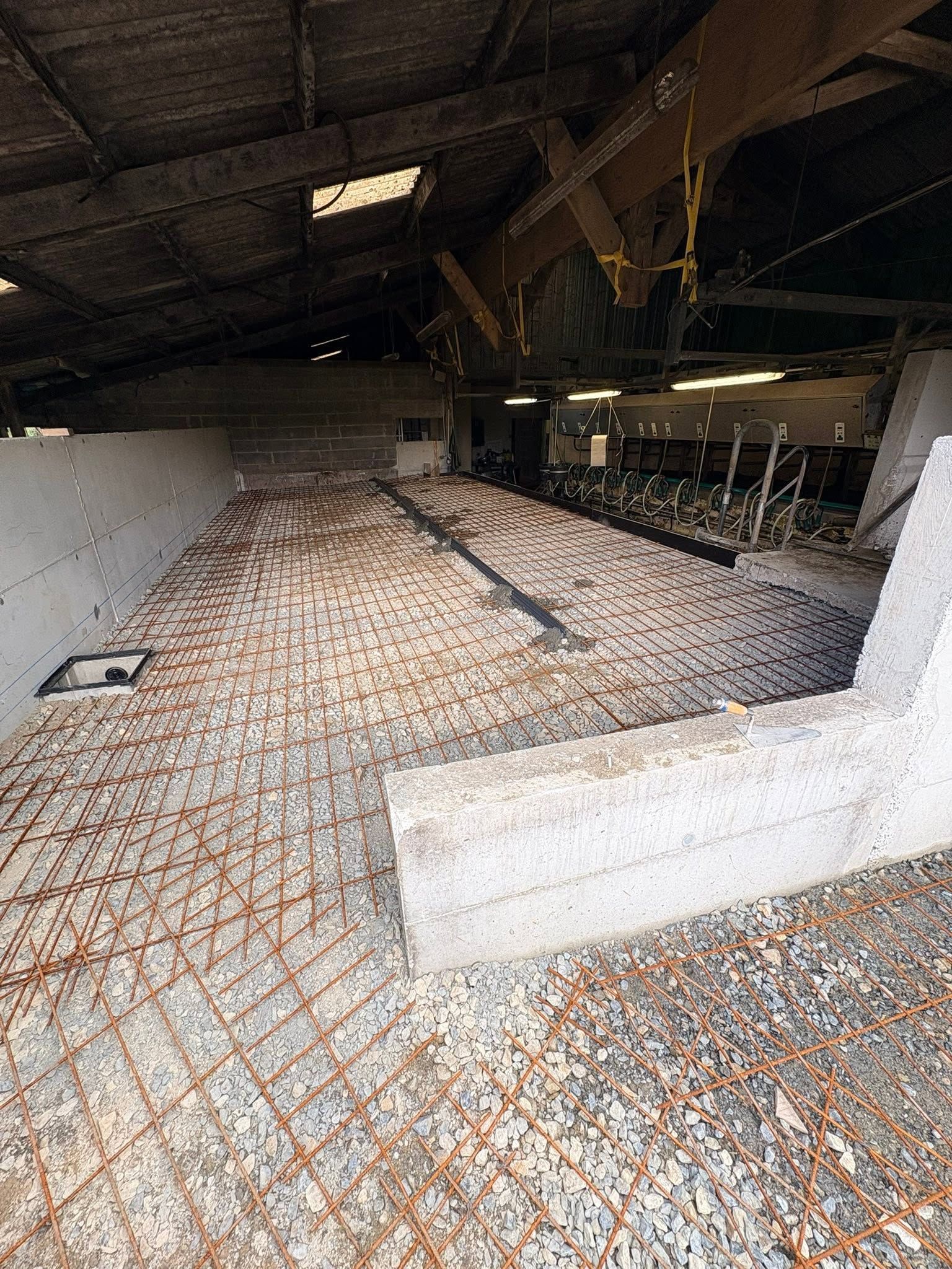 Intérieur d'un bâtiment agricole sombre avec un sol en béton en train d'être créé.