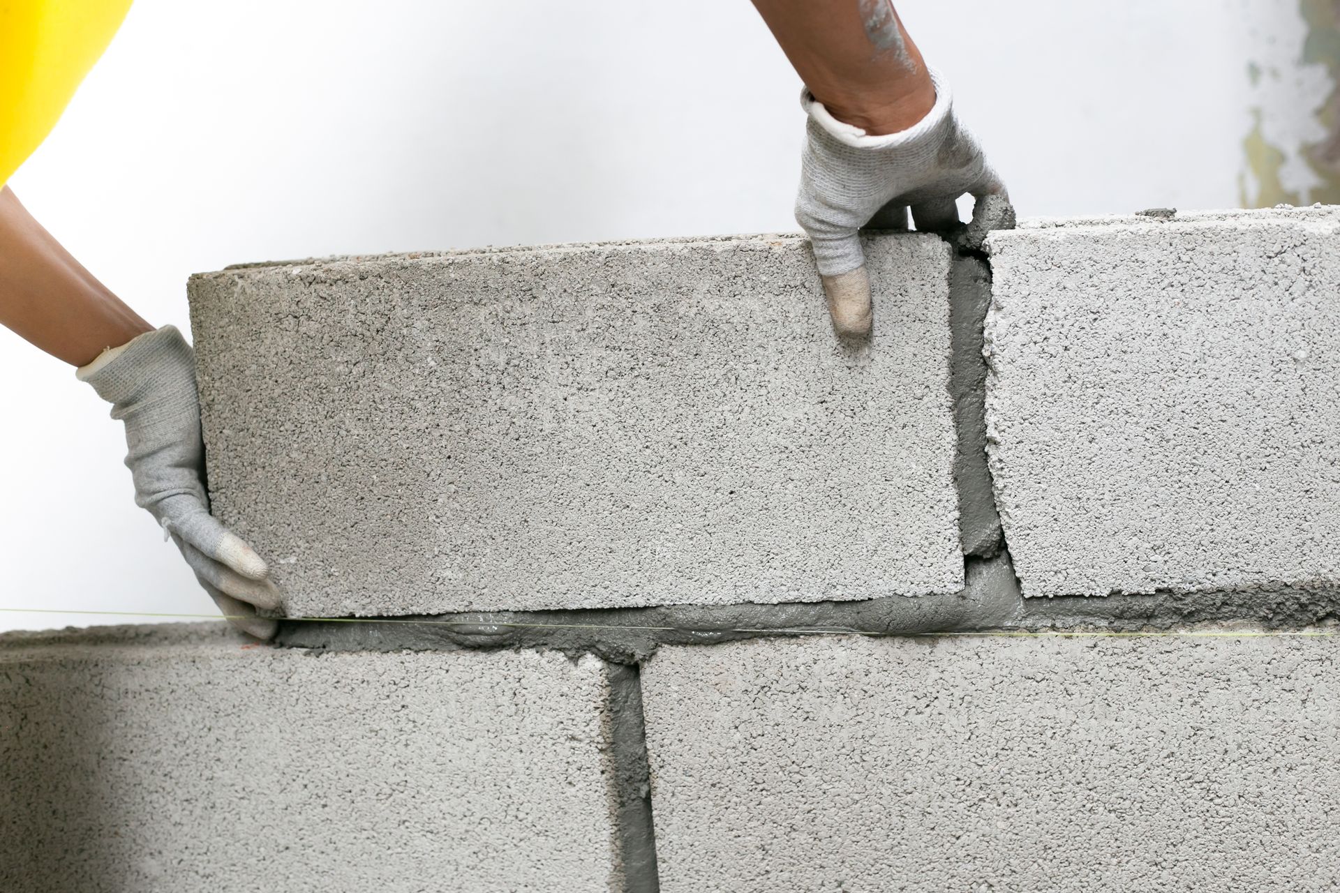 Des mains gantées construisent un mur en béton et parpaing
