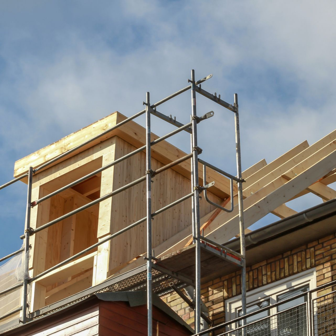 Échafaudages sur une maison en briques en construction avec une petite extension de toit en bois
