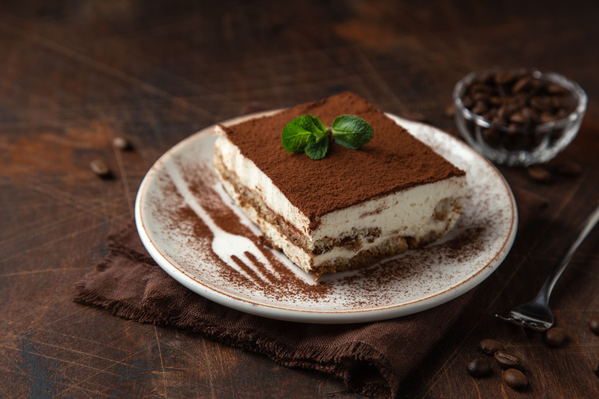 Une tranche de tiramisu sur une assiette blanche avec une fourchette.