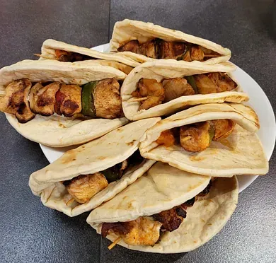 Un plato blanco cubierto con pan pita y brochetas de pollo.