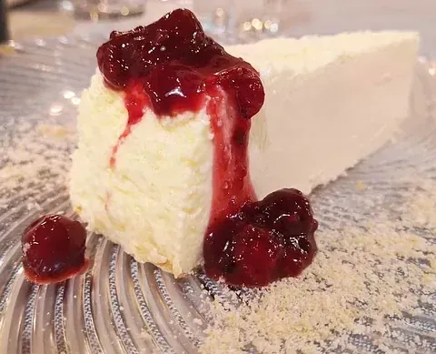 Una rebanada de tarta de queso con salsa de cerezas encima en un plato.