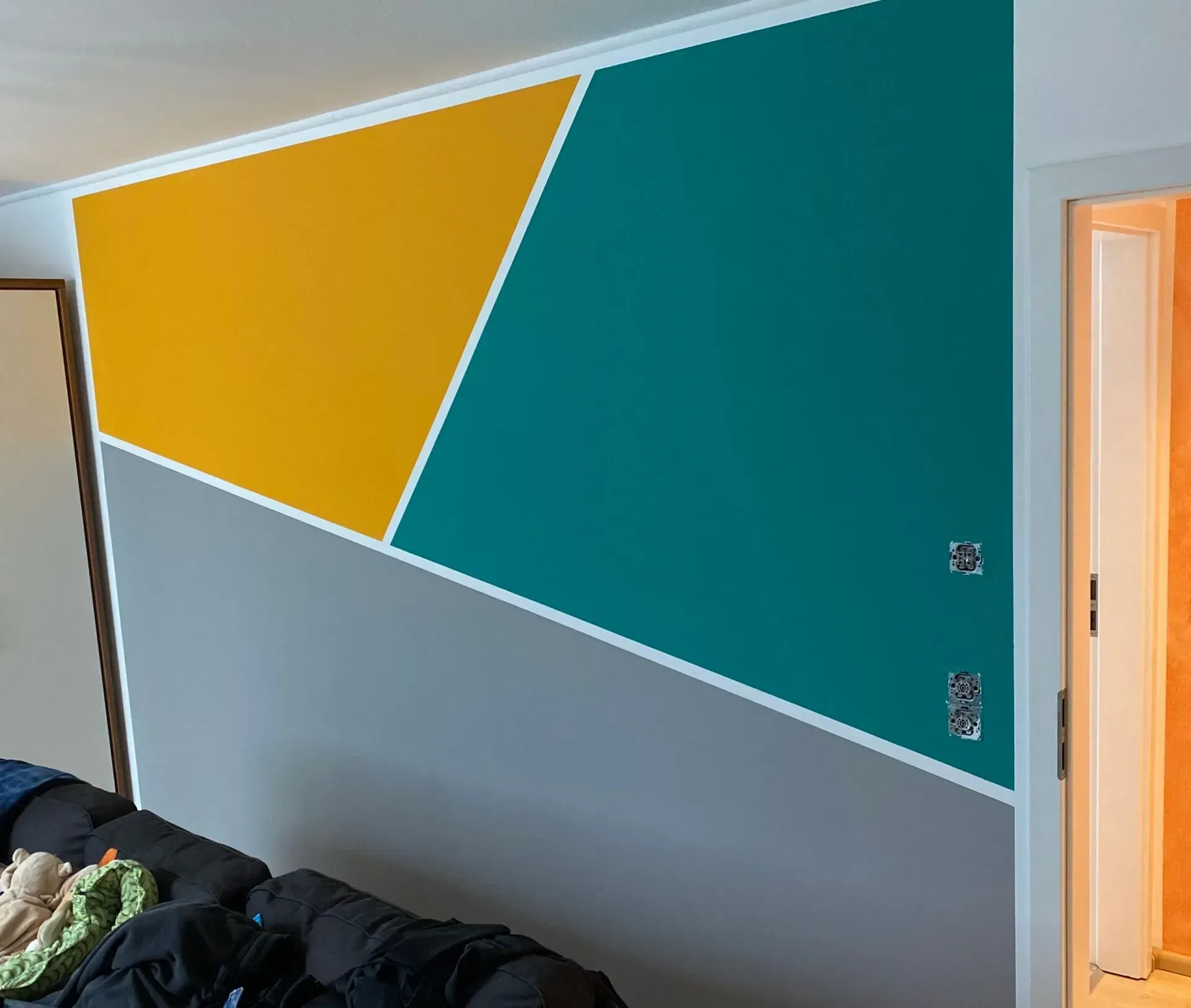 Wand mit geometrischen Farbflächen: gelb, petrol und grau