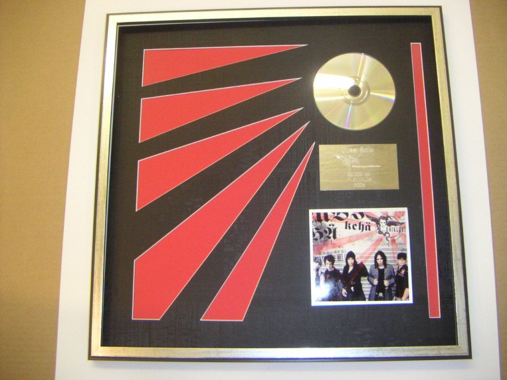 Kehyksiin pakattu musiikkipalkinto, jossa on kultainen CD, albumin kansi ja punainen kuvio mustalla taustalla.
