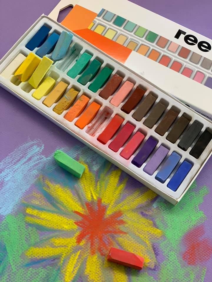 Pastelliliituja rasiassa, jossa on värikäs piirros kukasta violetilla paperilla.