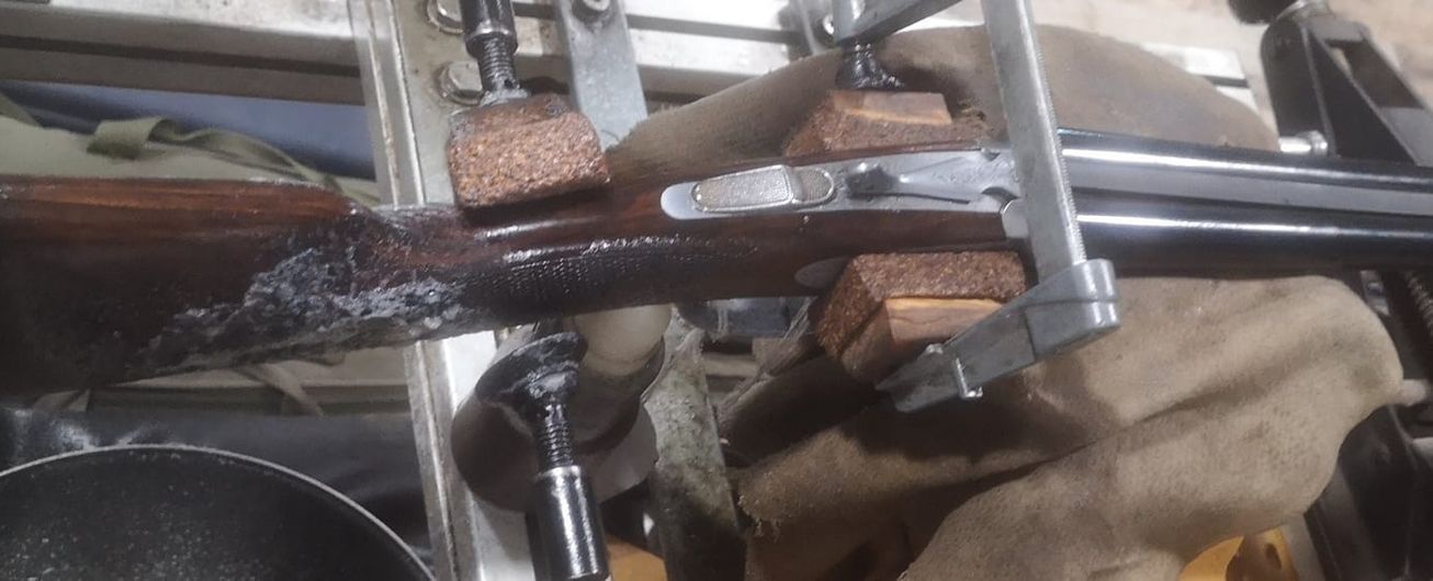 Arme avec une crosse abîmée fixée dans un étau, en cours de restauration