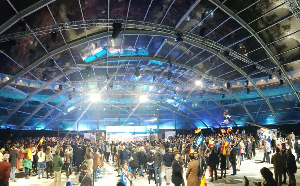 La multitud se congregó bajo el techo iluminado del estadio, con brillantes luces azules y un gran espacio abierto.