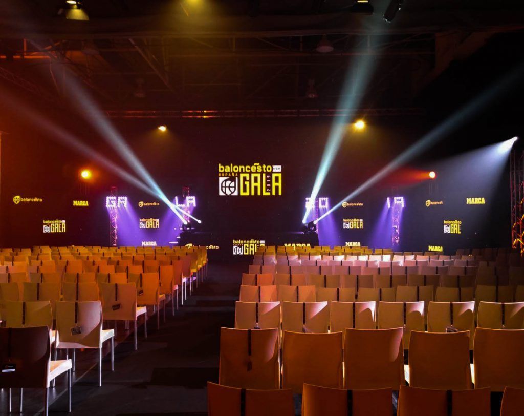 Auditorio vacío con filas de asientos color canela, luces de escenario y un telón de fondo brillantemente iluminado