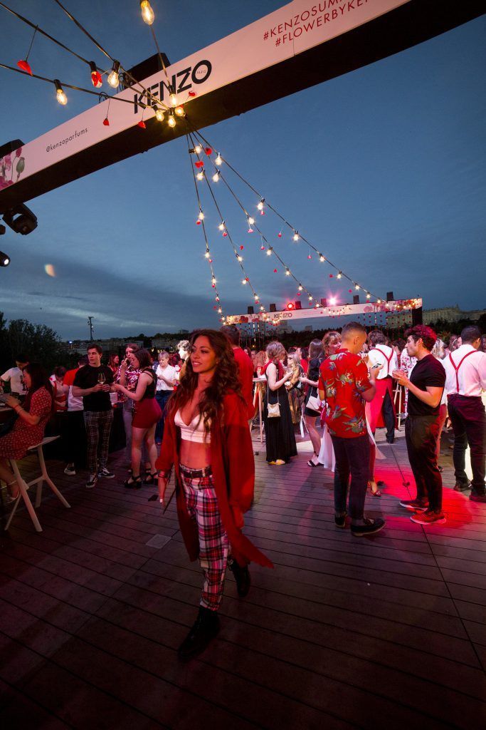 Gente bailando en un evento nocturno al aire libre bajo luces de guirnalda en una terraza en la azotea.