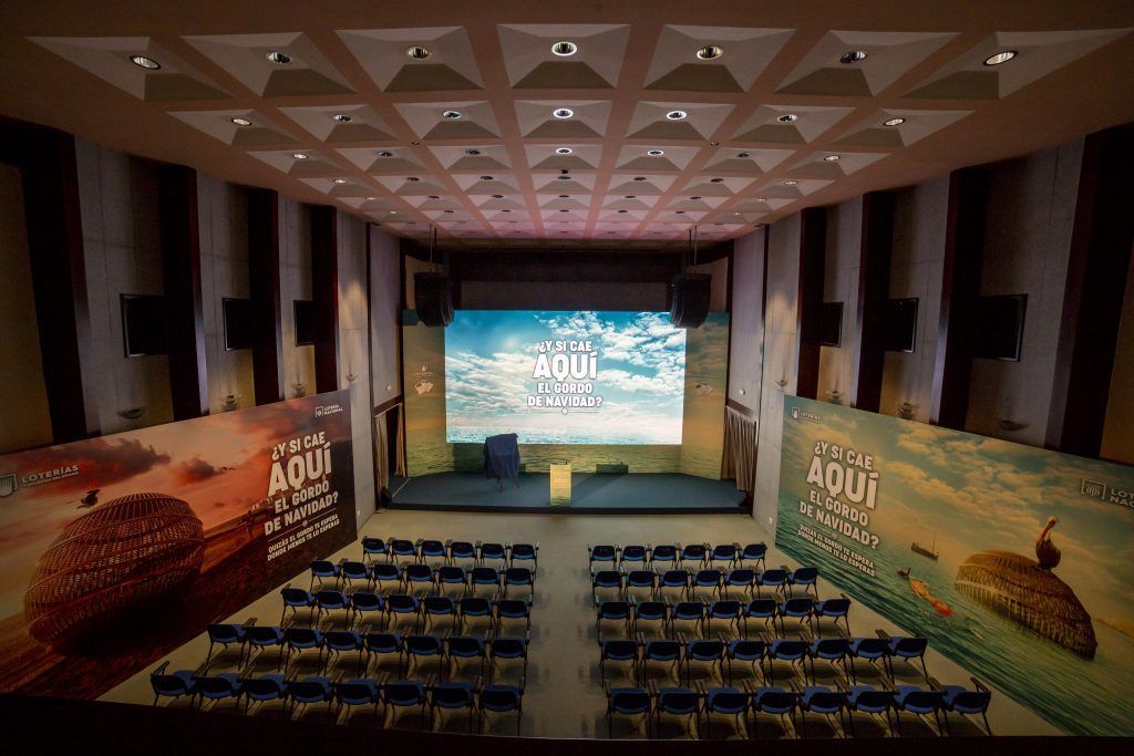 Auditorio de conferencias vacío con filas de sillas, escenario y grandes pancartas laterales con temática desértica.