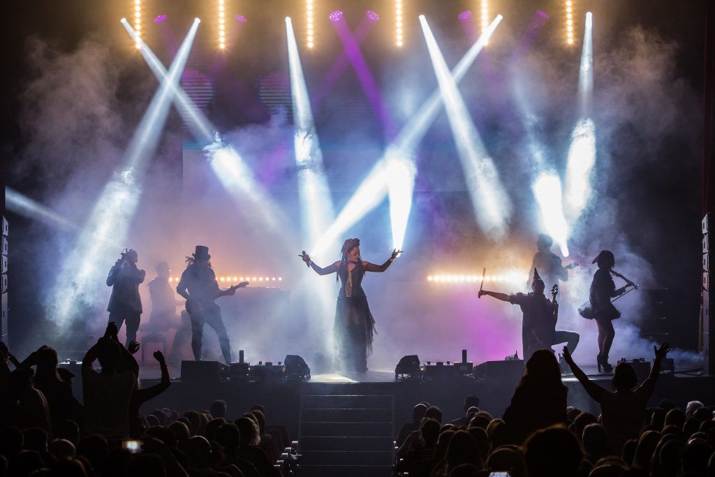 Silueta de una banda de rock actuando en el escenario bajo luces de concierto blancas y moradas brillantes y humo.