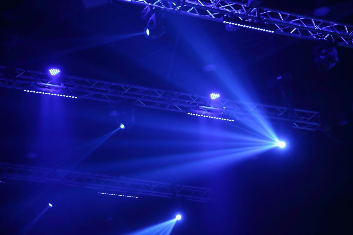 Focos azules iluminan el escenario a través de la neblina en un oscuro escenario de conciertos.