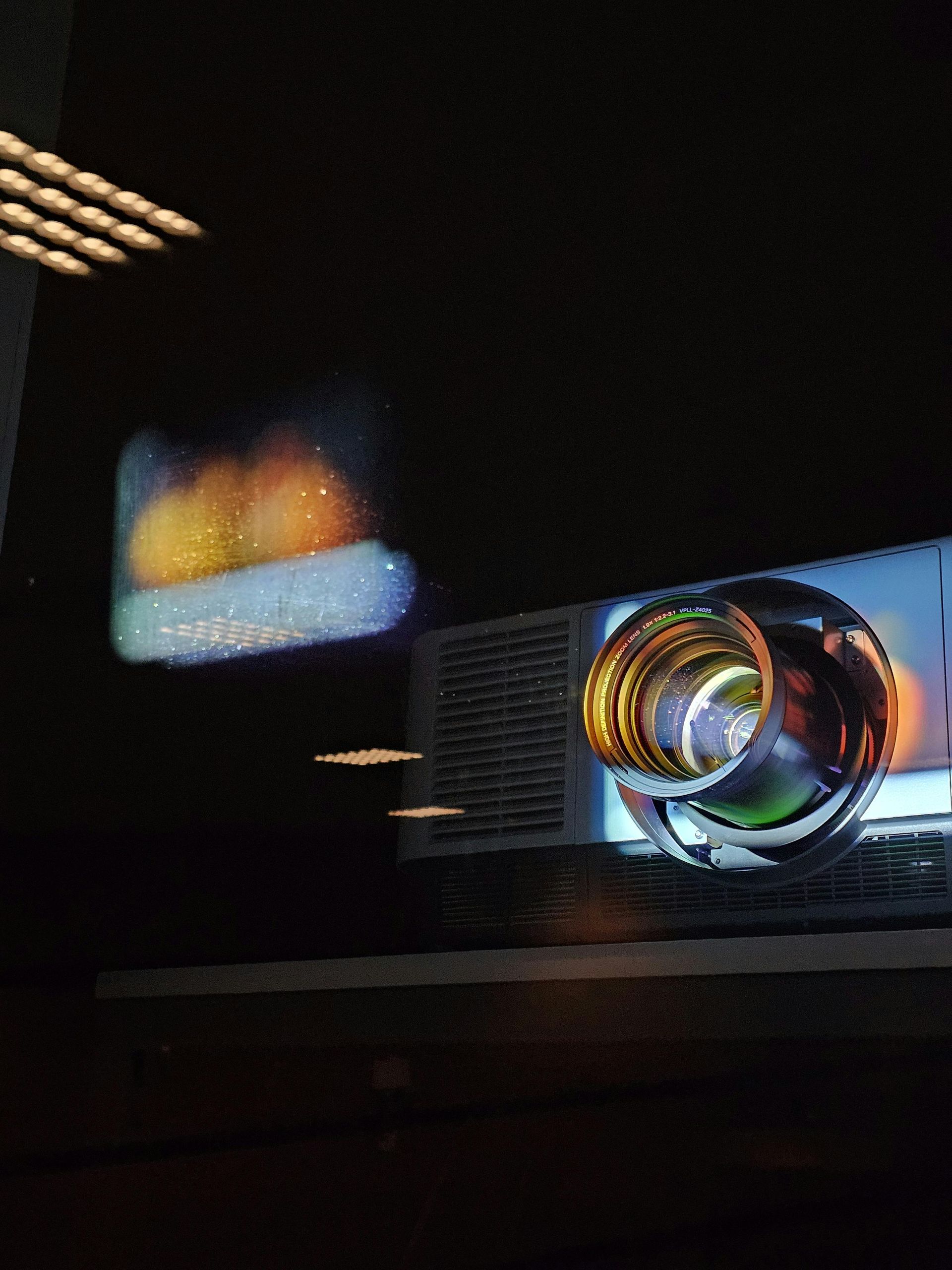 Lente de proyector colorida que brilla en una habitación oscura con suaves reflejos cerca.