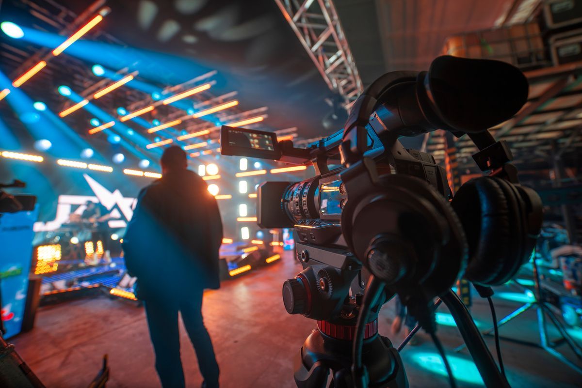 Una cámara de televisión graba a una persona en un estudio iluminado con luces de neón azules y naranjas.