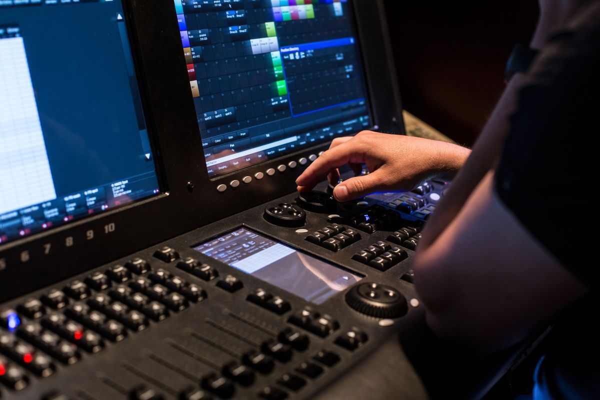 Persona manejando una consola de edición de video con dos monitores en una sala de control oscura.