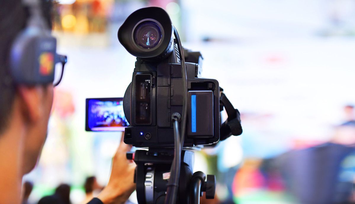 Cámara montada en un trípode filmando una escena interior luminosa, con una multitud borrosa y luces de colores al fondo.