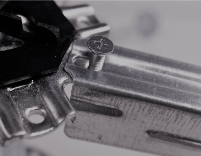 Primer plano de un soporte de metal con un tornillo parcialmente insertado, probablemente un componente mecánico.