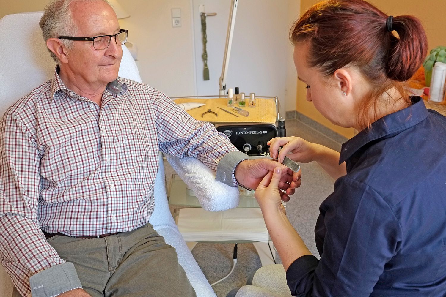 Ein älterer Mann lässt sich von einer Frau die Nägel machen.