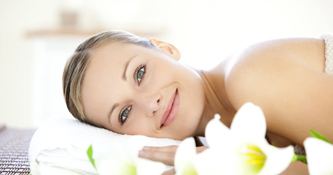 Eine Frau liegt auf einem Massagetisch mit weißen Blumen.