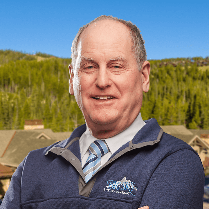 Man in blue sweater, mountains in background, smiling at the camera. Logo on the sweater.