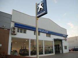 Un concesionario de coches Peugeot con un cartel delante.