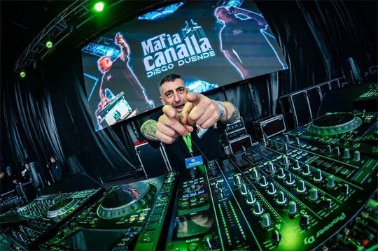 Un DJ está sentado en una mesa frente a una pantalla grande.
