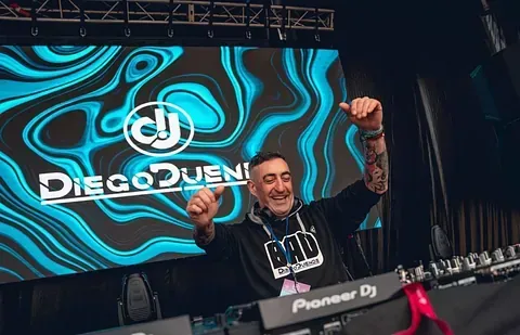 Un DJ está sentado en una mesa frente a una pantalla grande.