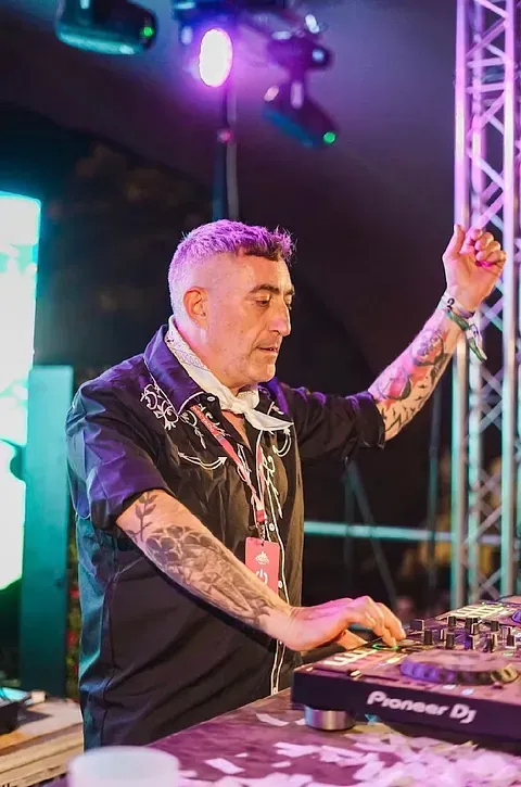 Un hombre con tatuajes está tocando un set de DJ en una habitación oscura.