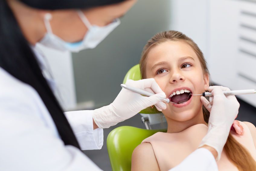 Una niña está sentada en una silla dental mientras un dentista le examina los dientes.