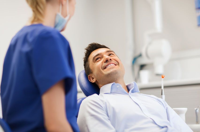 Un hombre está sentado en una silla dental hablando con un dentista.