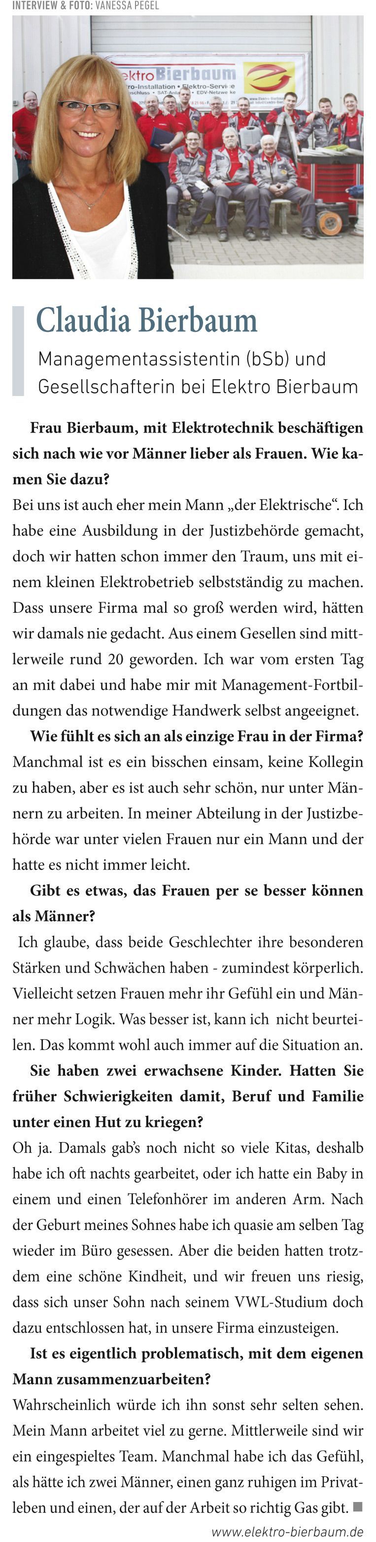 Eine Frau in einer schwarzen Jacke und einem weißen Hemd steht vor einem großen Schild.