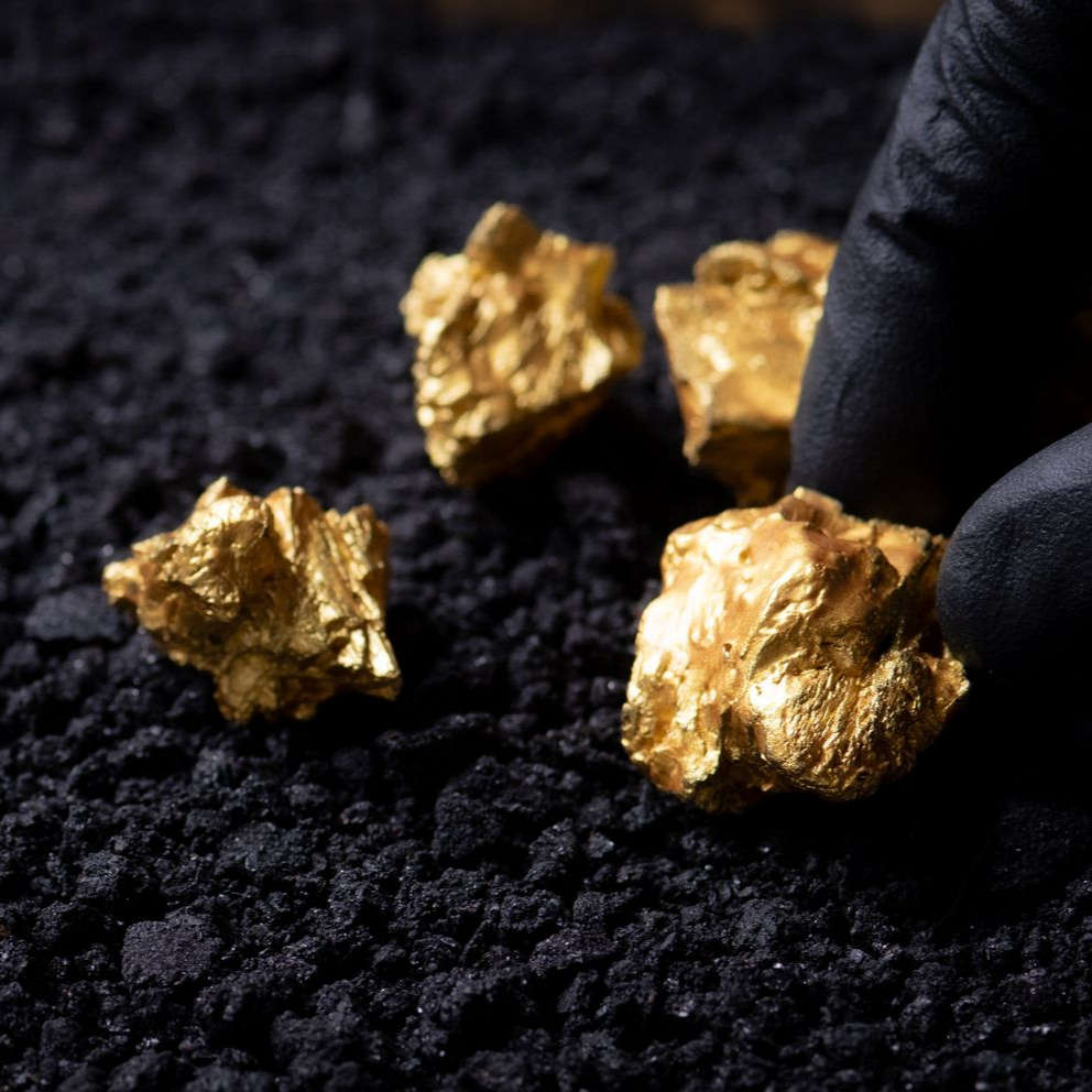 Main gantée tenant des pépites d'or sur une surface sombre et texturée