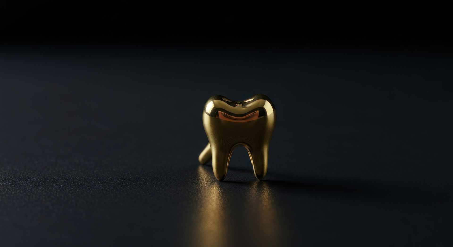 Petit objet en forme de dent en or sur fond sombre, doucement éclairé par le haut