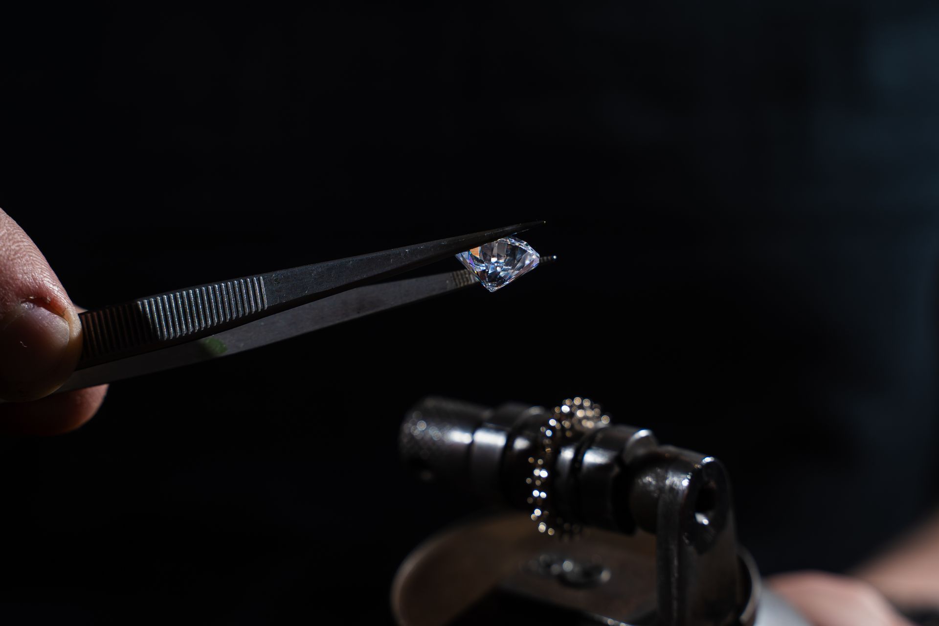 Un outil de bijoutier maintient un minuscule cristal au-dessus de la platine d'un microscope dans un laboratoire obscur.