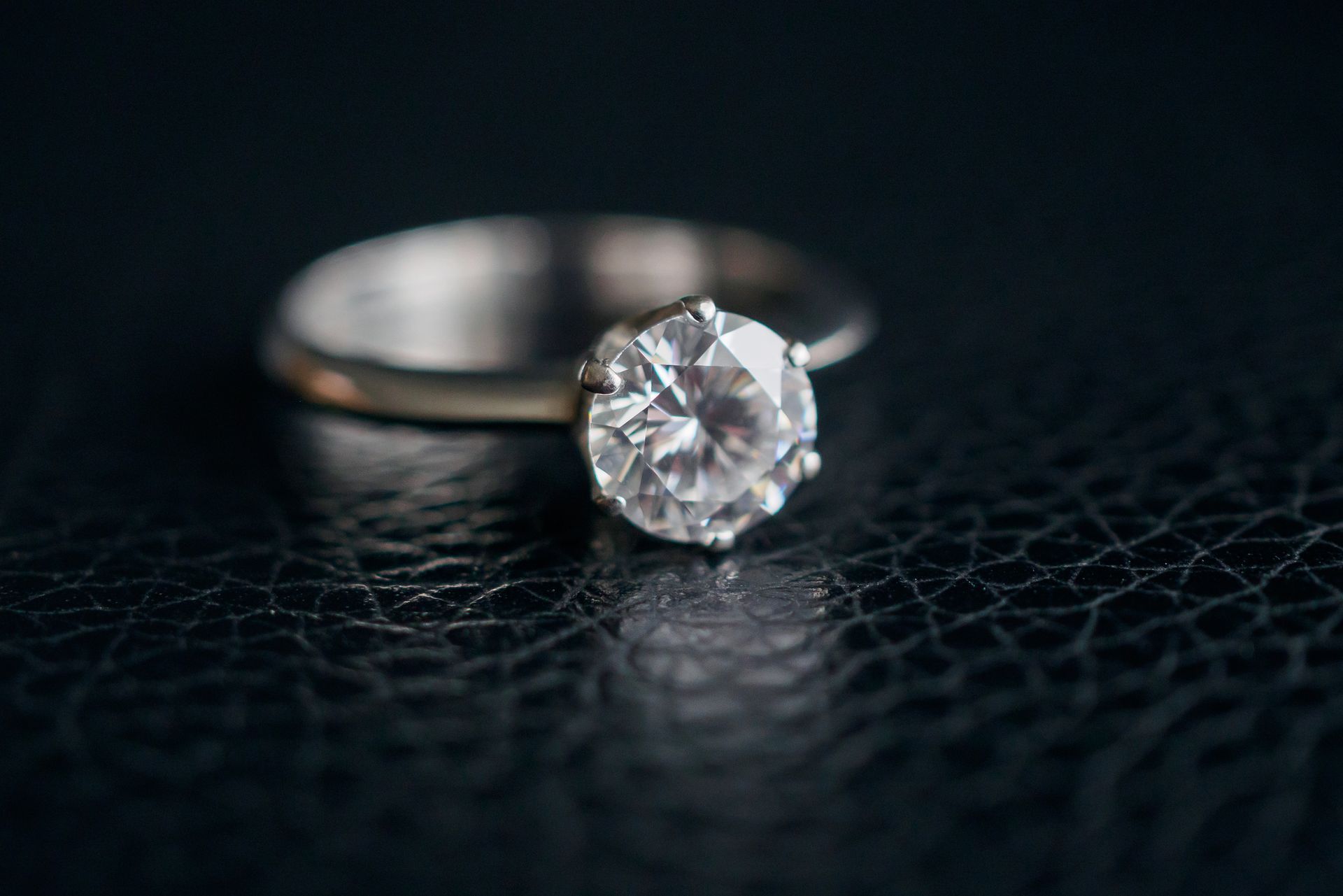 Bague de fiançailles en diamant sur une surface texturée sombre, avec un anneau flou en arrière-plan