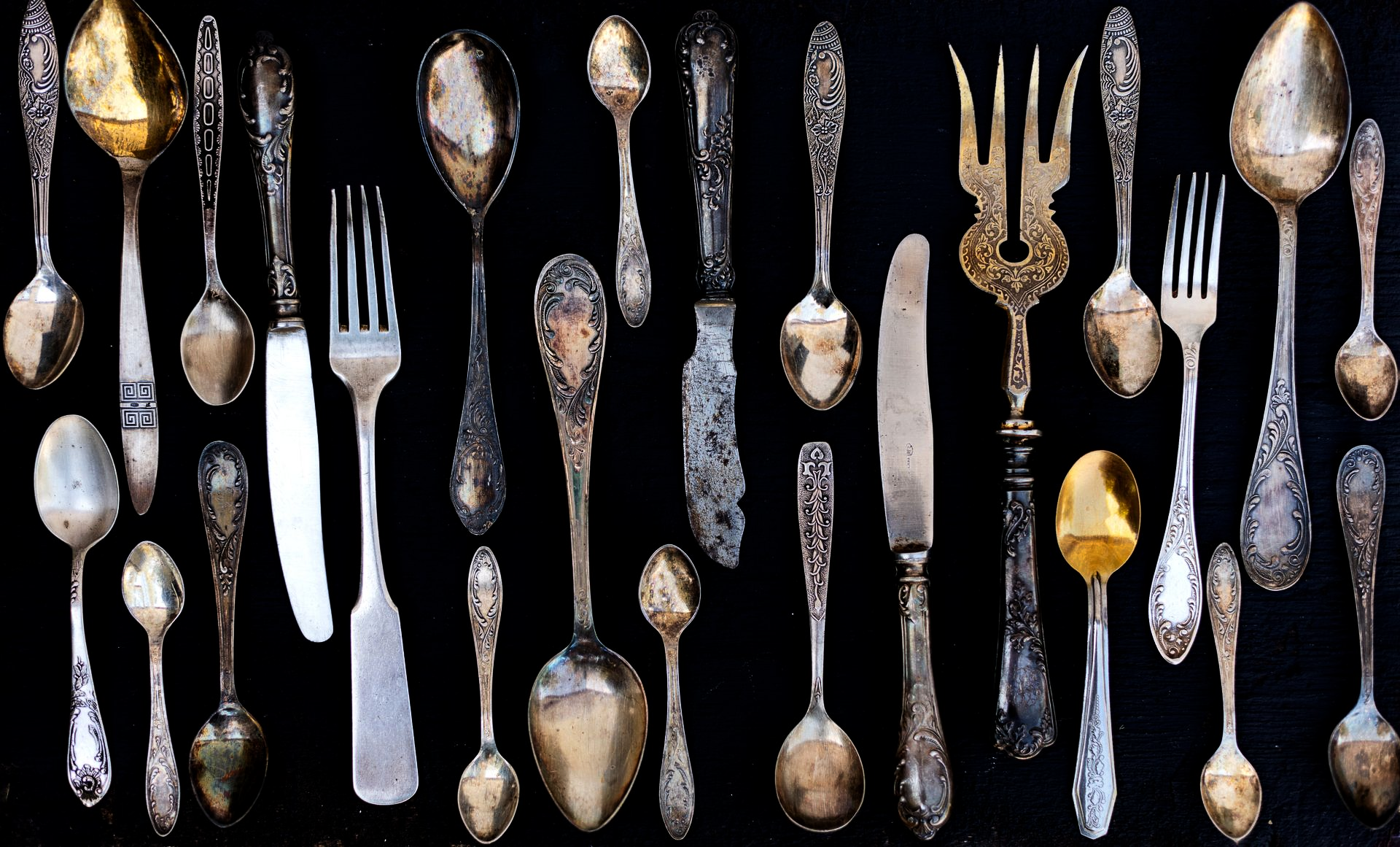 Assortiment de couverts anciens en argent et en or disposés verticalement sur un fond noir