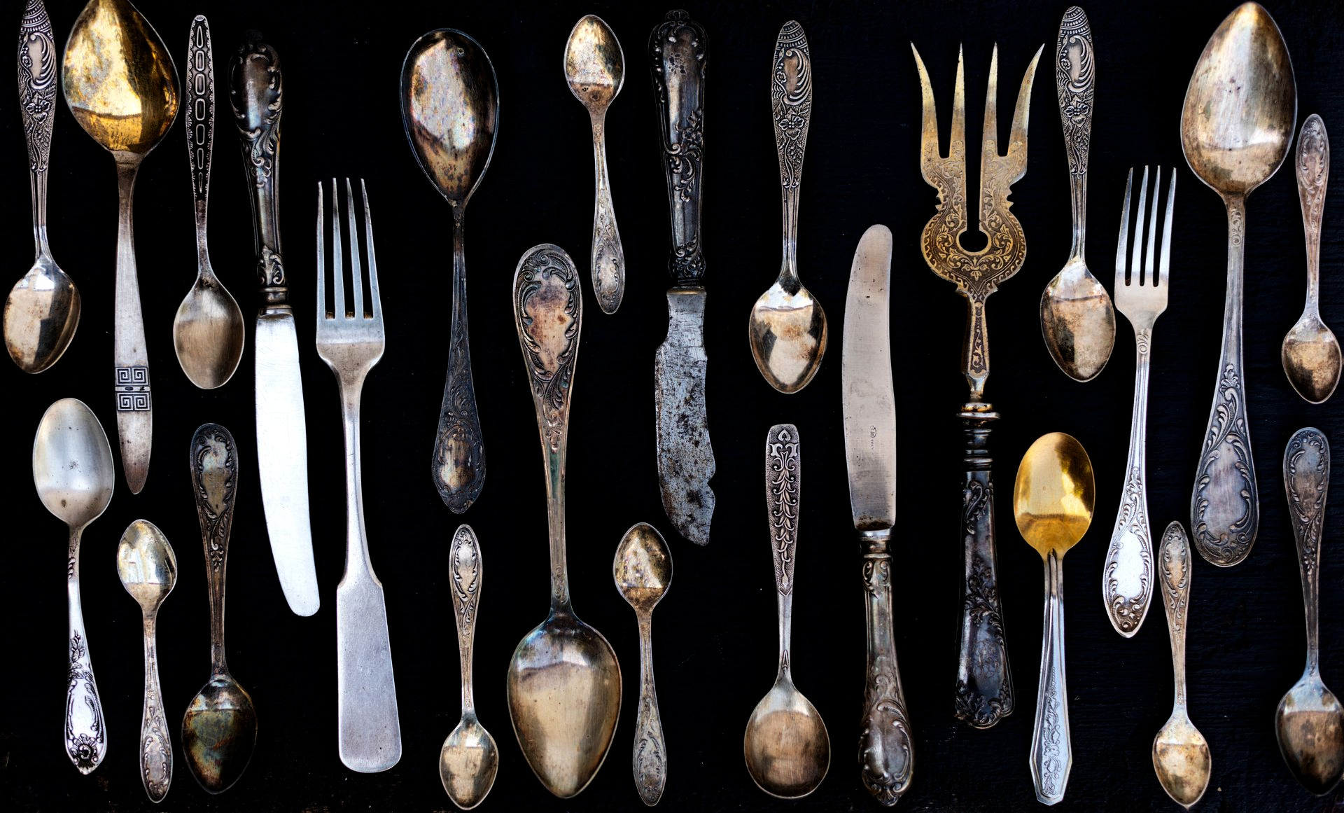 Assortiment de cuillères et fourchettes en argent vintage disposées sur un fond noir, avec quelques pièces dorées.