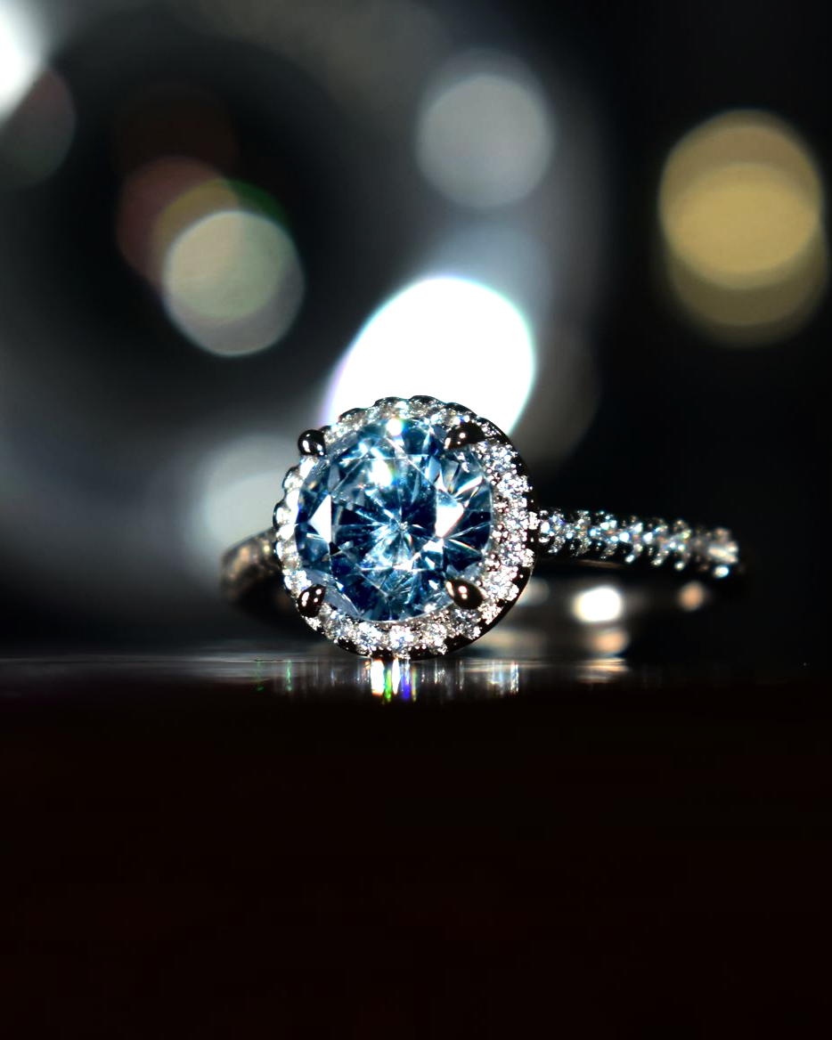 Bague en diamant orné d'une pierre précieuse bleue sur une surface sombre et réfléchissante, éclairée par une douce lumière.