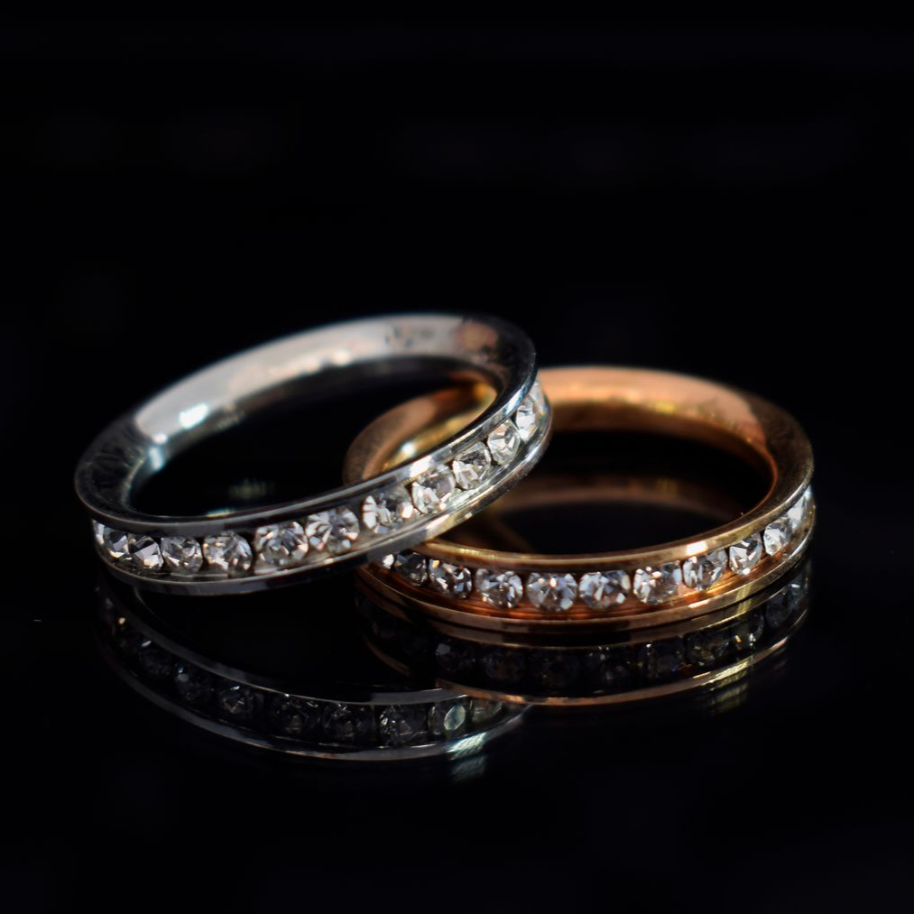 Deux alliances en diamant entrelacées, l'une en argent et l'autre en or rose, sur une surface noire réfléchissante
