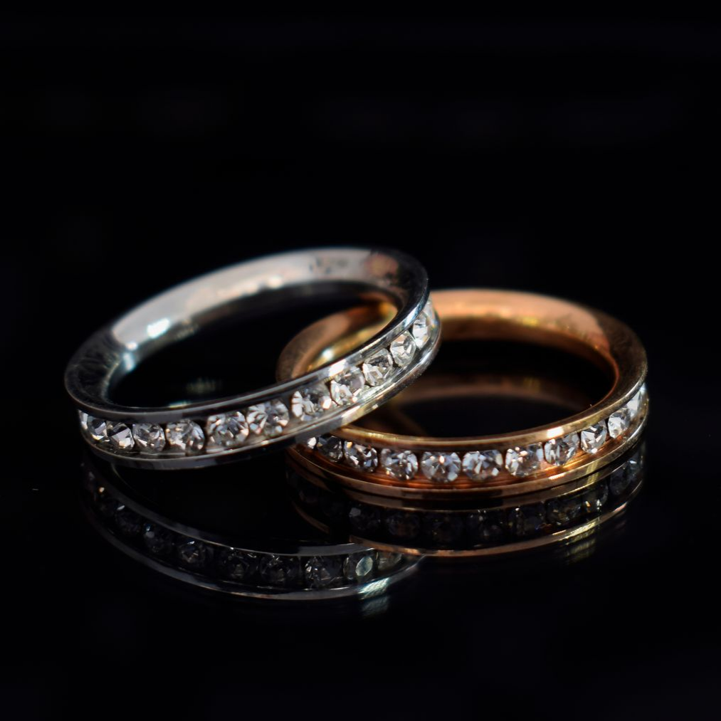 Deux anneaux entrelacés, l'un en argent et l'autre en or, ornés de petits diamants sur fond noir.