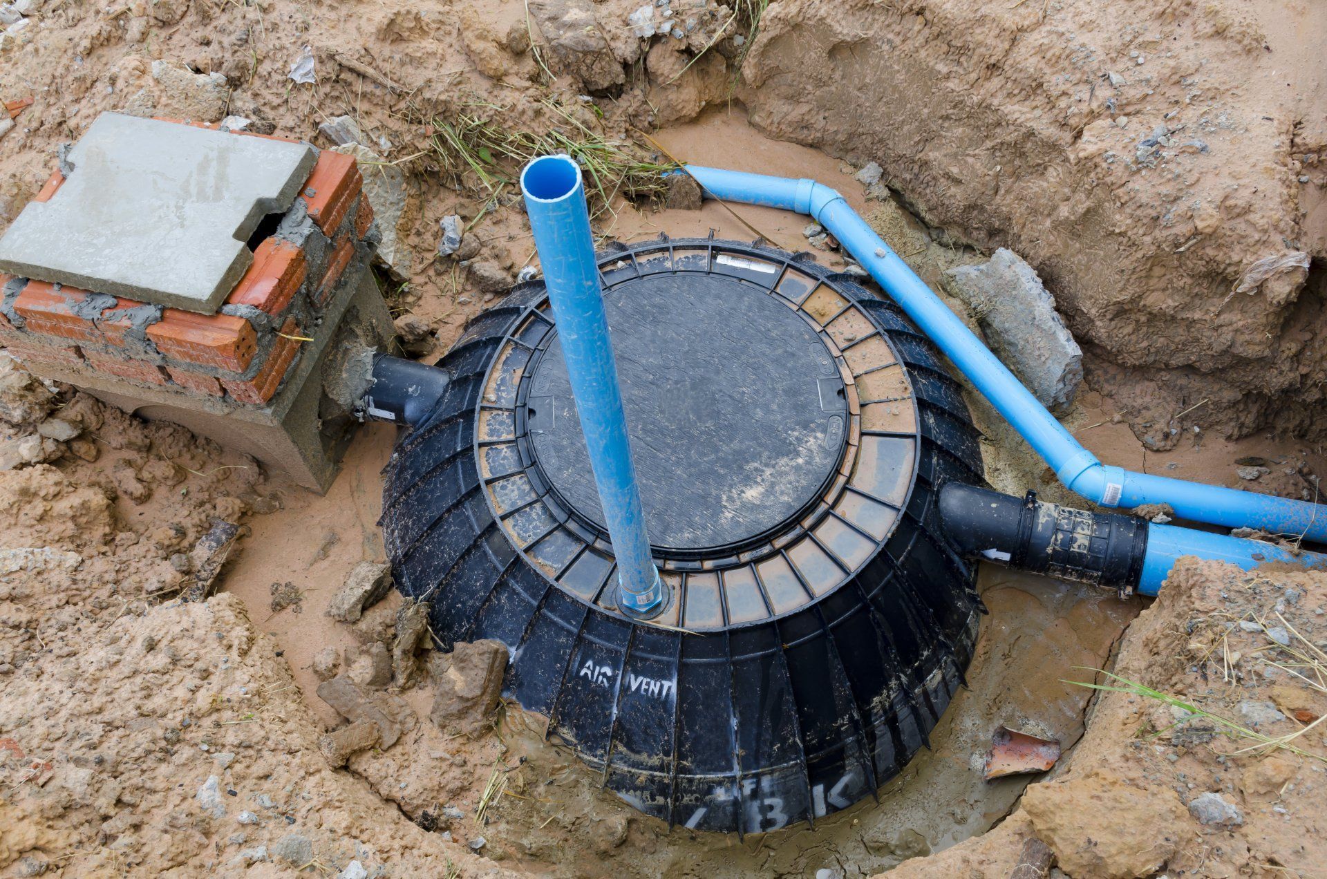 Réservoir d'eau souterrain et tuyaux bleus dans un chantier de terrassement avec un boîtier utilitaire en briques